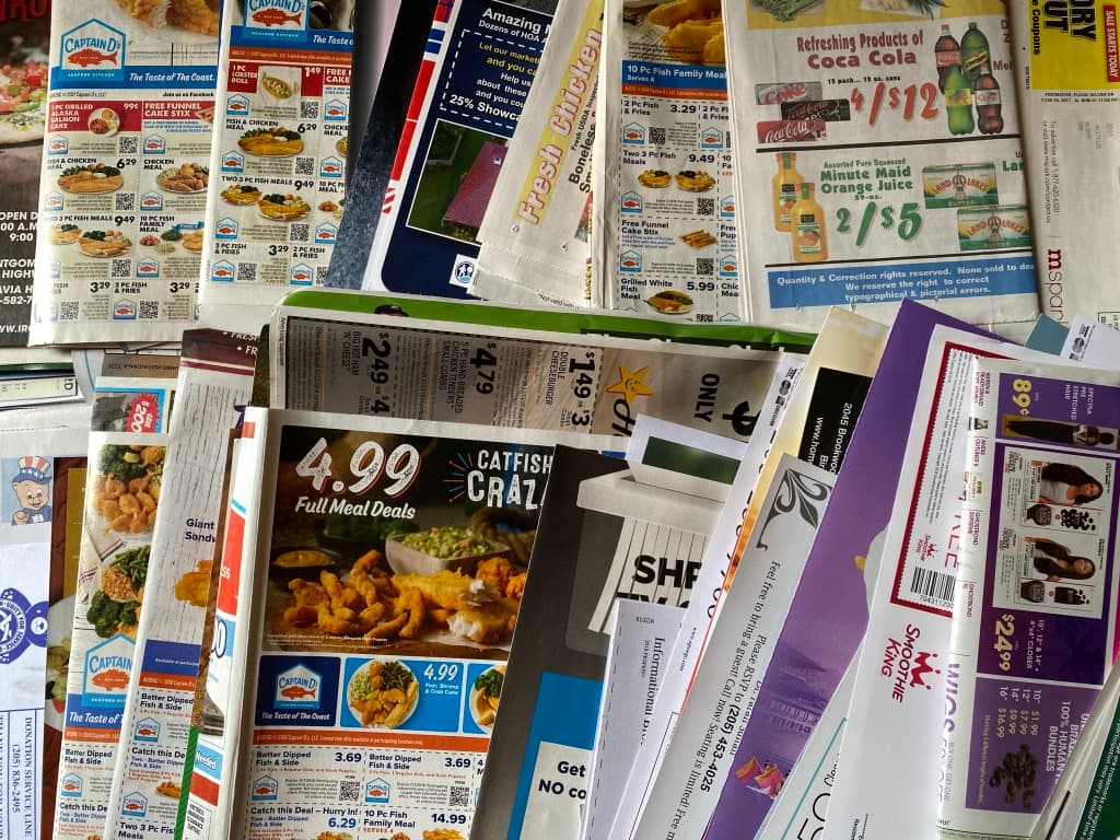 A week of EDDM flyers spread on a table: grocery circulars, restaurant menus and service ads